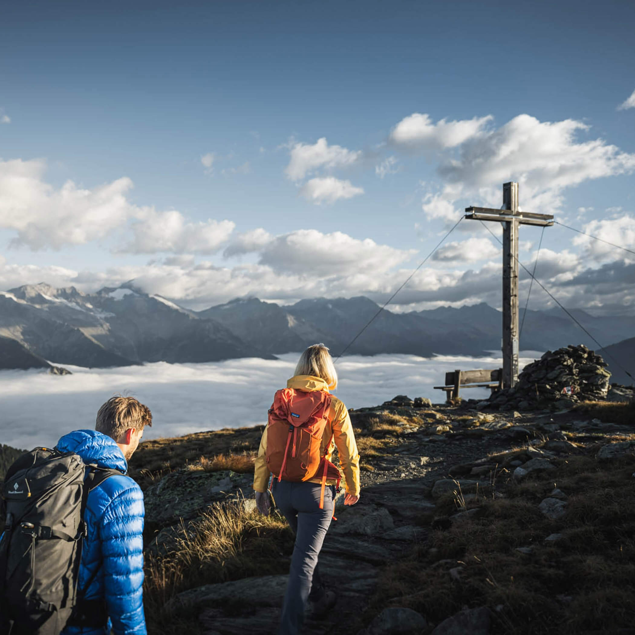 Hikers reach a summit cross with a mountain panorama in the Vedrette di Ries-Aurina Nature Park - OLM Nature Escape