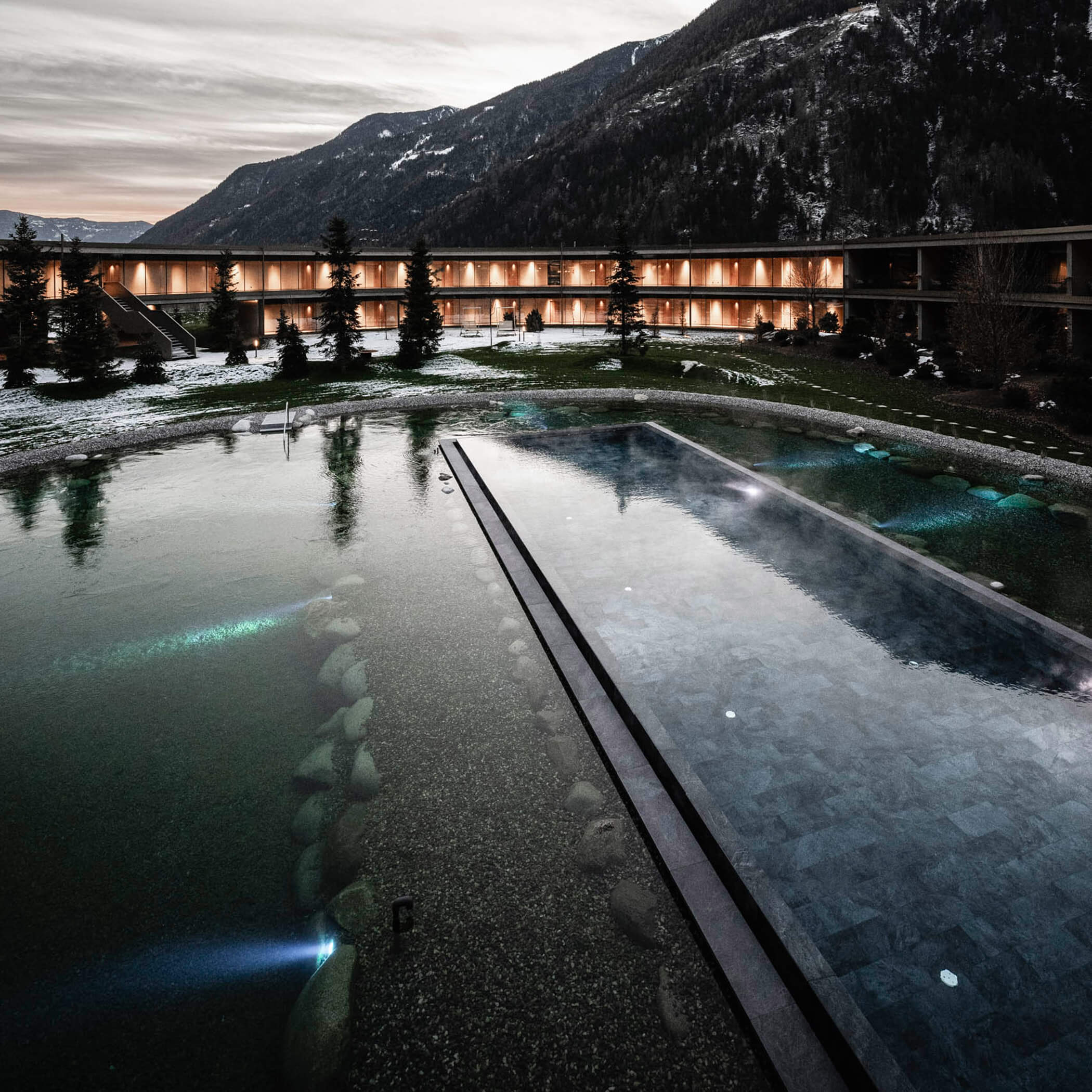 Beleuchteter Außenpool und Naturbadeteich am Abend - OLM Nature Escape