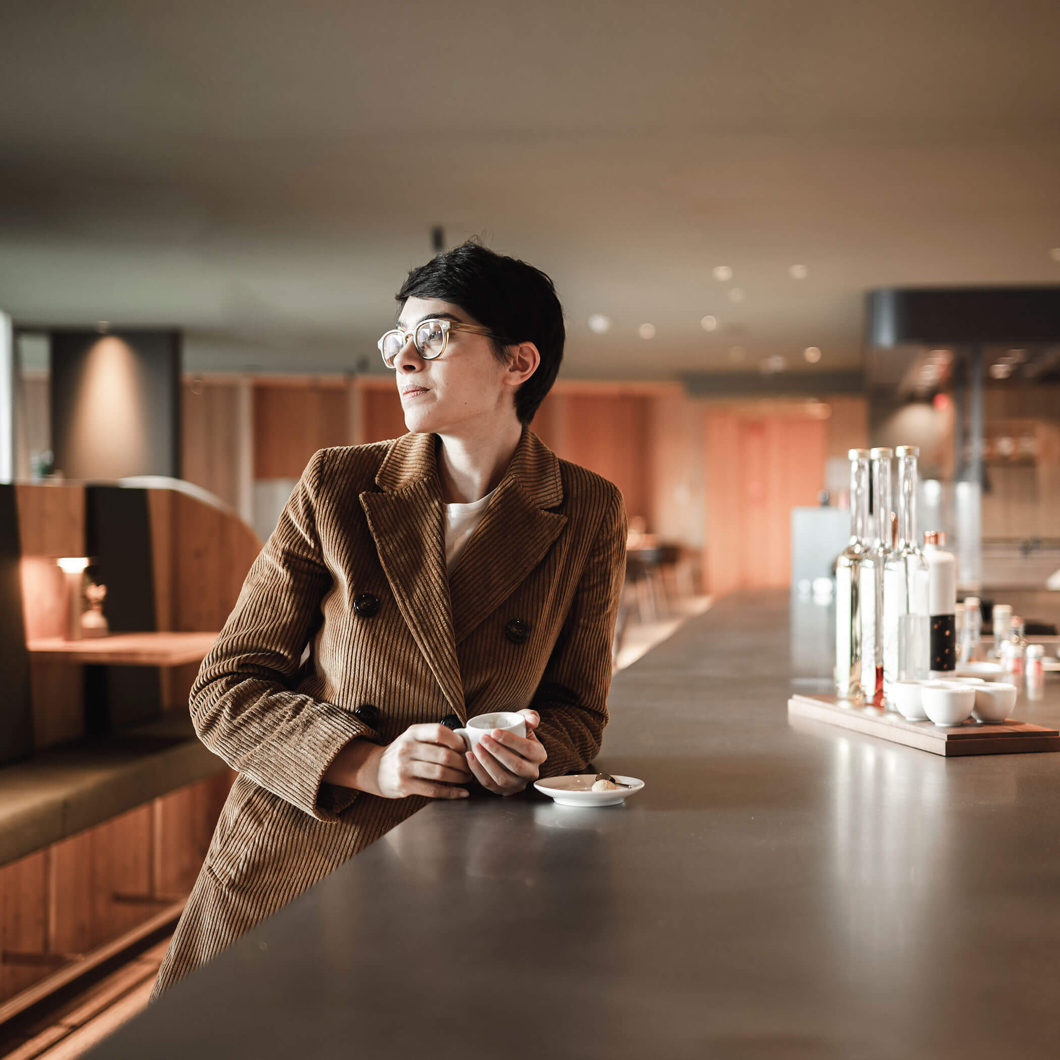 Una donna appoggiata al bar con un caffè in mano - OLM Nature Escape