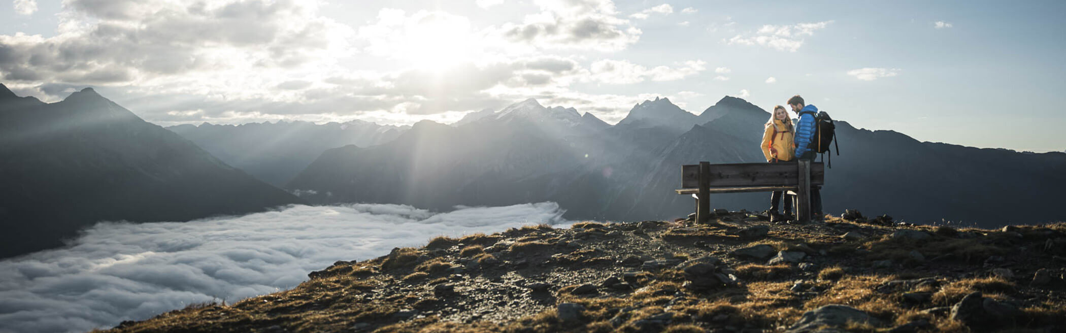 Coppia in piedi su una panchina che guarda la valle coperta di nebbia e il panorama montuoso - OLM Nature Escape