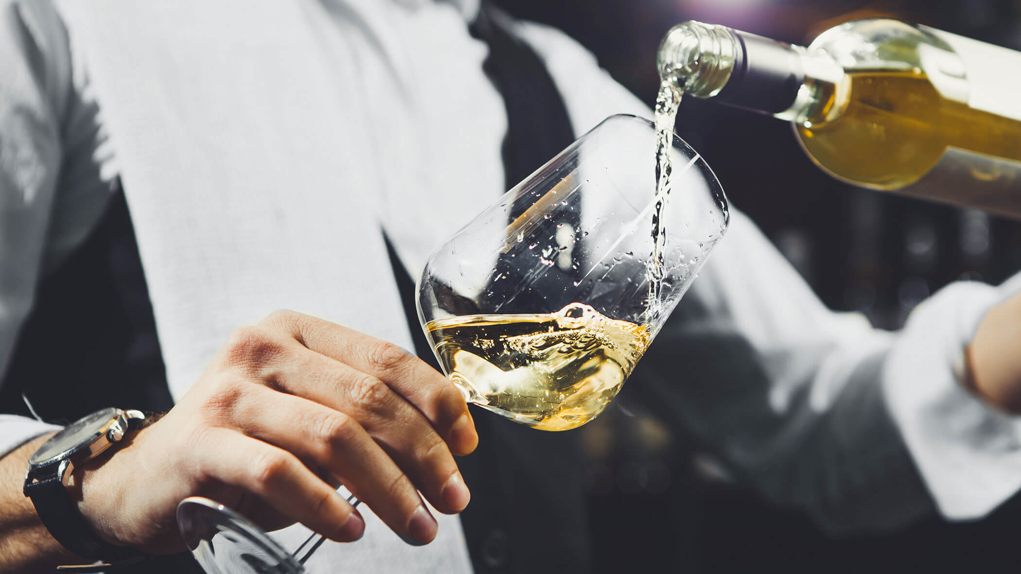 Mann gißt Weißwein ins Glas bei 